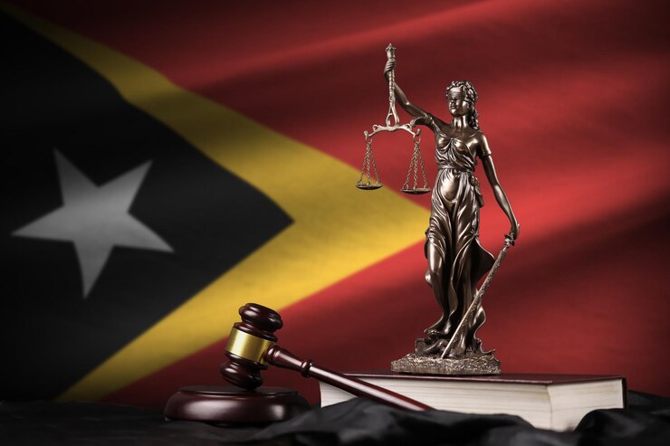 Foto bandeira de timor-leste com a estátua da constituição da justiça e martelo do juiz na cortina preta conceito de julgamento e culpa