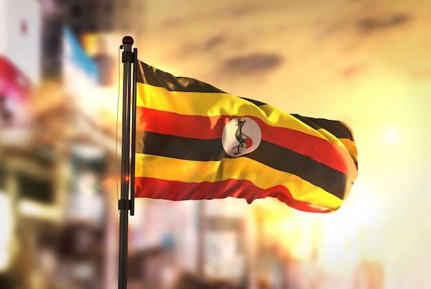 Foto bandeira de uganda contra a cidade fundo borrado no amanhecer luz de fundo