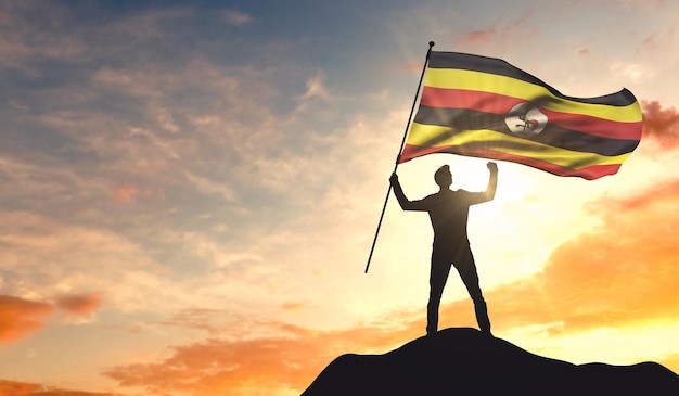 Bandeira de Uganda sendo acenada por um homem comemorando o sucesso no topo de uma montanha 3D Rendering