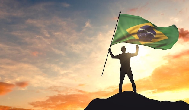 Bandeira do Brasil sendo acenada por um homem comemorando o sucesso no topo de uma montanha 3D Rendering