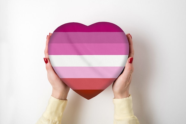Bandeira do orgulho LGBT lésbica em uma caixa de forma de coração nas mãos femininas. Símbolo do orgulho. Vista do topo