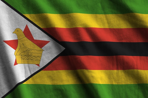 Foto bandeira do zimbábue com grandes dobras acenando sob a luz do estúdio dentro de casa os símbolos oficiais e cores no banner