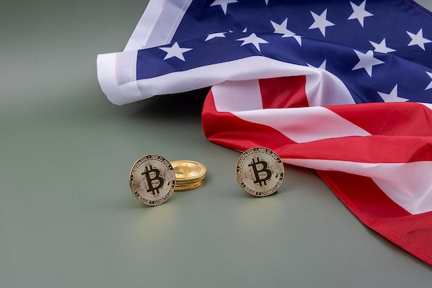Bandeira dos EUA e ao lado alguns bitcoins em uma mesa verde