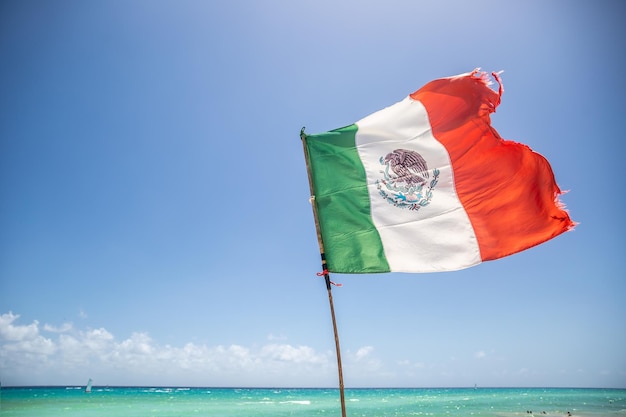 Bandeira mexicana parcialmente rasgada pelo vento que sopra do mar turquesa do Caribe