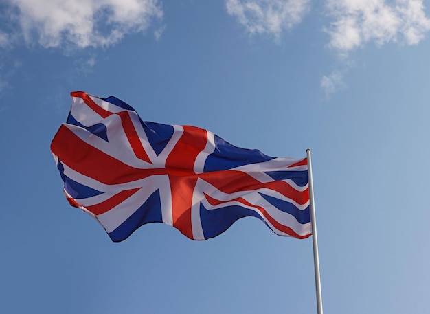 Bandeira nacional da Grã-Bretanha voando e balançando ao vento sobre o céu azul claro, símbolo do patriotismo britânico, ângulo baixo, vista lateral