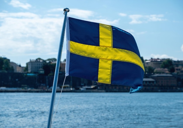 Bandeira nacional da Suécia acenando borrão edifícios à beira-mar de Estocolmo e céu azul