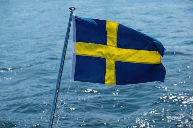 Bandeira nacional da Suécia acenando no mastro do barco desfocando o fundo da água do mar