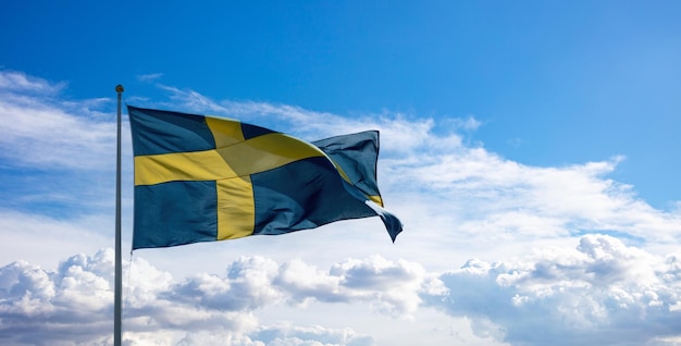 Bandeira nacional da Suécia acenando sobre um mastro de bandeira azul céu nublado