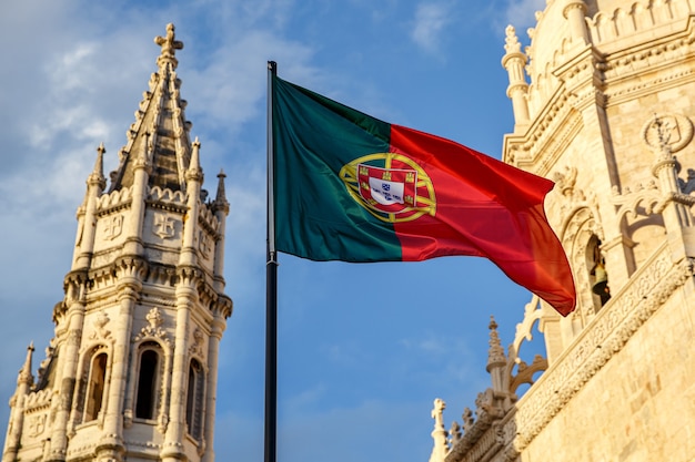 Bandeira portuguesa acenando na frente de um céu azul e um mosteiro.