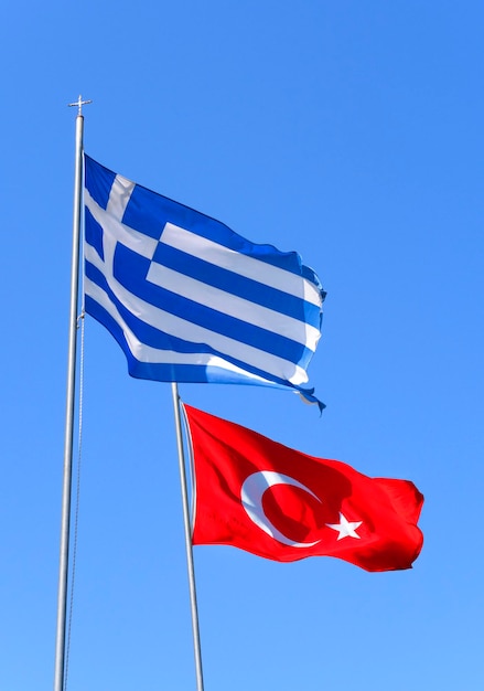 Bandeiras da grécia e da turquia estão voando ao vento contra o céu azul