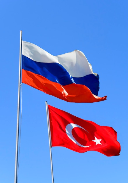 Bandeiras da Rússia e da Turquia estão voando ao vento contra o céu azul