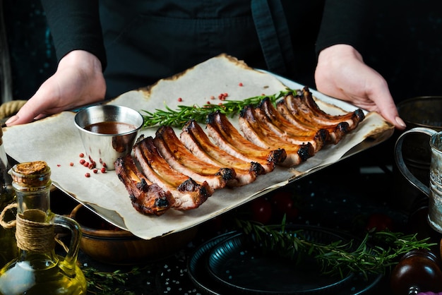 Bandeja de barbacoa con jugosas costillas de cerdo al horno en manos del chef sobre fondo rústico de madera