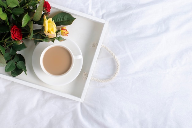 Bandeja con café y un ramo de flores sobre una cama blanca, copie el espacio.