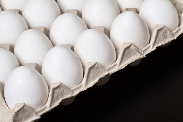 Bandeja de cartón con huevos de gallina blanca sobre un fondo oscuro