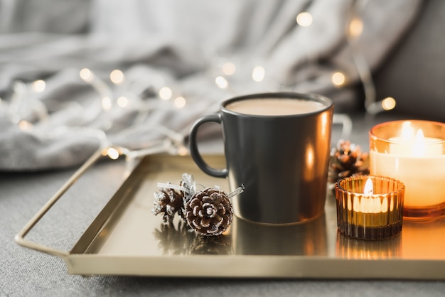 Bandeja com café em uma caneca preta, velas aromáticas acesas e pinhas decorativas