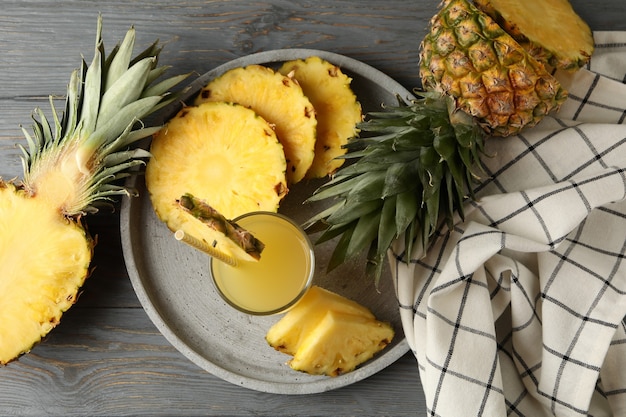 Bandeja com fatias de abacaxi e copo de suco no fundo de madeira, vista superior