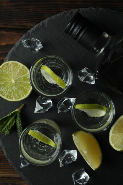 Bandeja com garrafa e doses de vodka, limão e gelo na mesa de madeira