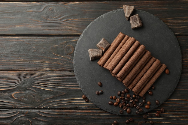 Bandeja com rolinhos de wafer de chocolate, grãos de café e chocolate em madeira