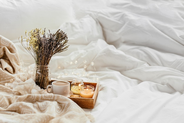 Bandeja de café e velas com manta quente sobre roupa de cama branca. Café da manhã na cama.