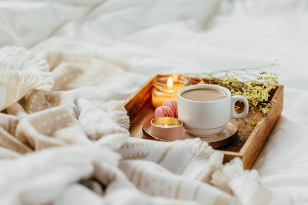 Bandeja de café e velas com manta quente sobre roupa de cama branca. Café da manhã na cama.