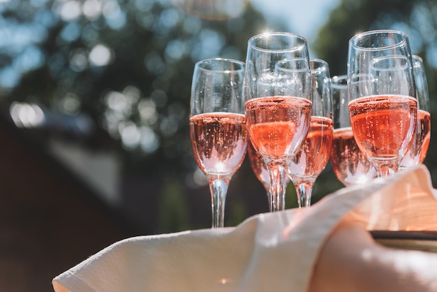 Bandeja de copos de vinho espumante rosa verão para os convidados em uma recepção de casamento nos raios de sol