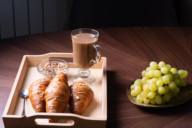 Bandeja de madeira com uma xícara de café, muesli e com croissants frescos em uma mesa marrom