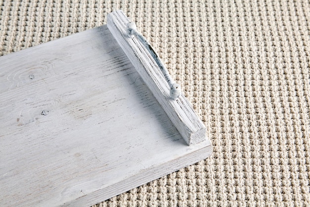 bandeja de madeira pintada de branco com alças de metal contra o fundo de um plaid bege tricotado