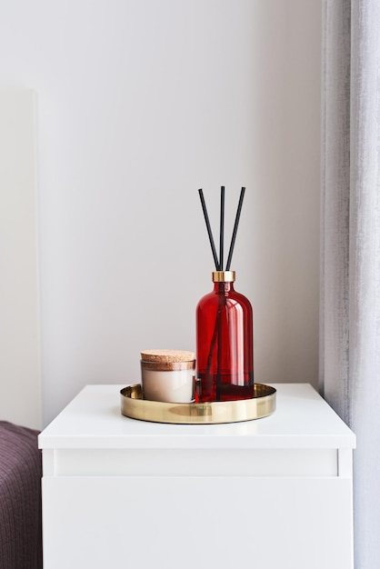 Bandeja de metal com vela de aroma e garrafa de difusor de fragrância de quarto em uma mesa de cabeceira no quarto