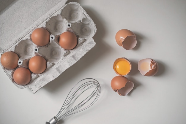Bandeja de ovos crus frescos e de shell de ovo quebrado no fundo branco.