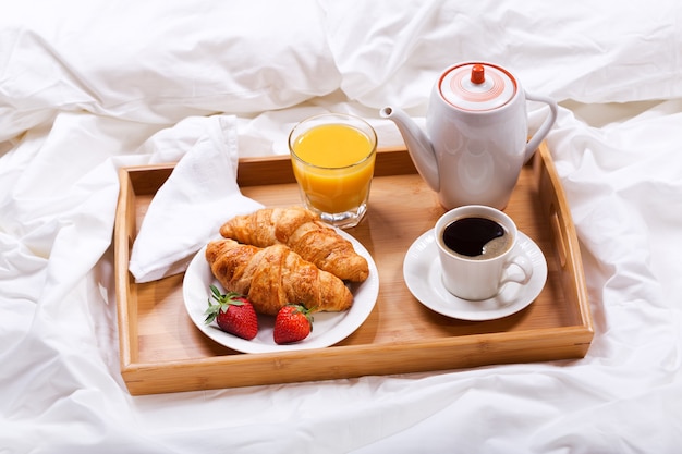 Bandeja de desayuno en la cama café croissants jugo y fresas frescas