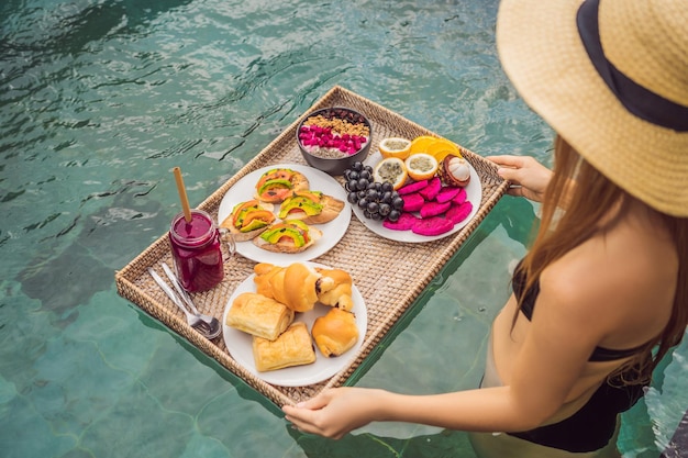 Bandeja de desayuno en la piscina desayuno flotante en hotel de lujo chica relajándose en la piscina