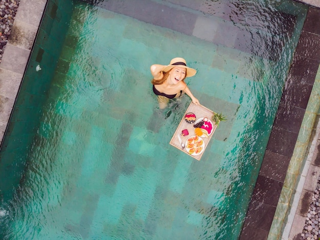 Bandeja de desayuno en la piscina desayuno flotante en hotel de lujo chica relajándose en la piscina