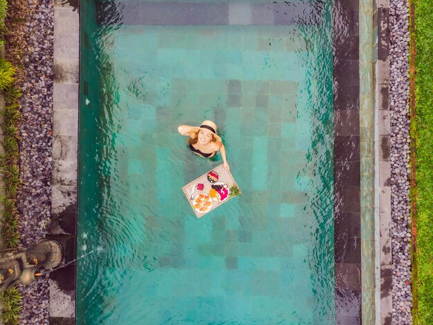 Bandeja de desayuno en la piscina desayuno flotante en hotel de lujo chica relajándose en la piscina