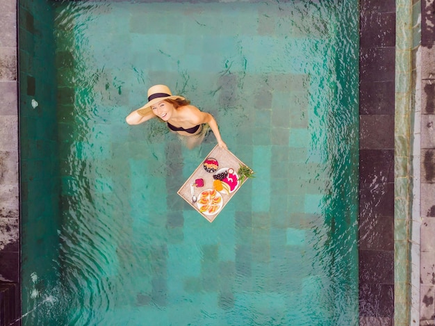 Bandeja de desayuno en la piscina desayuno flotante en hotel de lujo chica relajándose en la piscina