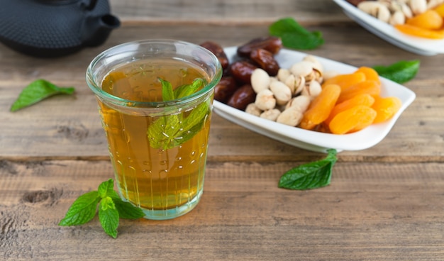 Bandeja de frutos secos con dátiles, pistachos y orejones con vaso de té sobre fondo de madera. Copie el espacio.