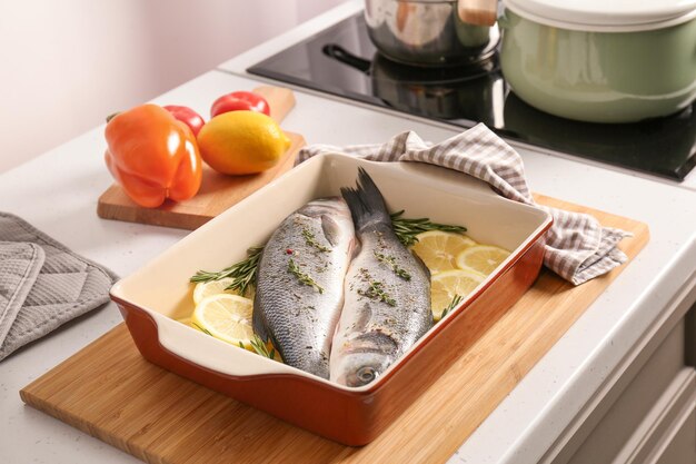 Bandeja para hornear con rodajas de limón de pescado crudo y hierbas en la mesa de la cocina