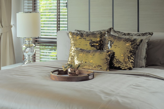 Bandeja de madera con almohadas doradas en la cama.