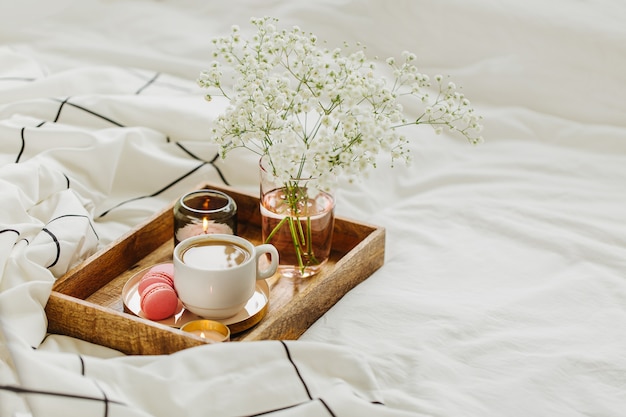 Bandeja de madera con café y velas con flores en la cama. Desayuno en la cama. Concepto Hygge.