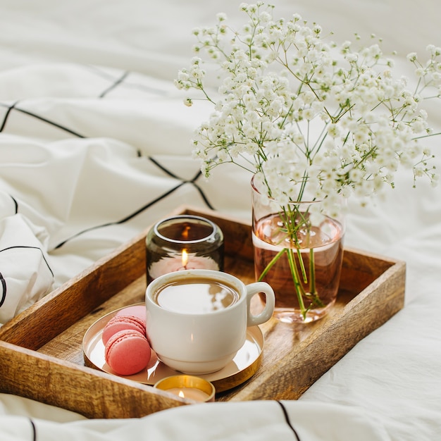 Bandeja de madera con café y velas con flores en la cama. Desayuno en la cama. Concepto Hygge.