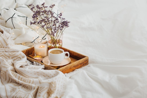 Bandeja de madera con café y velas con flores en la cama.
