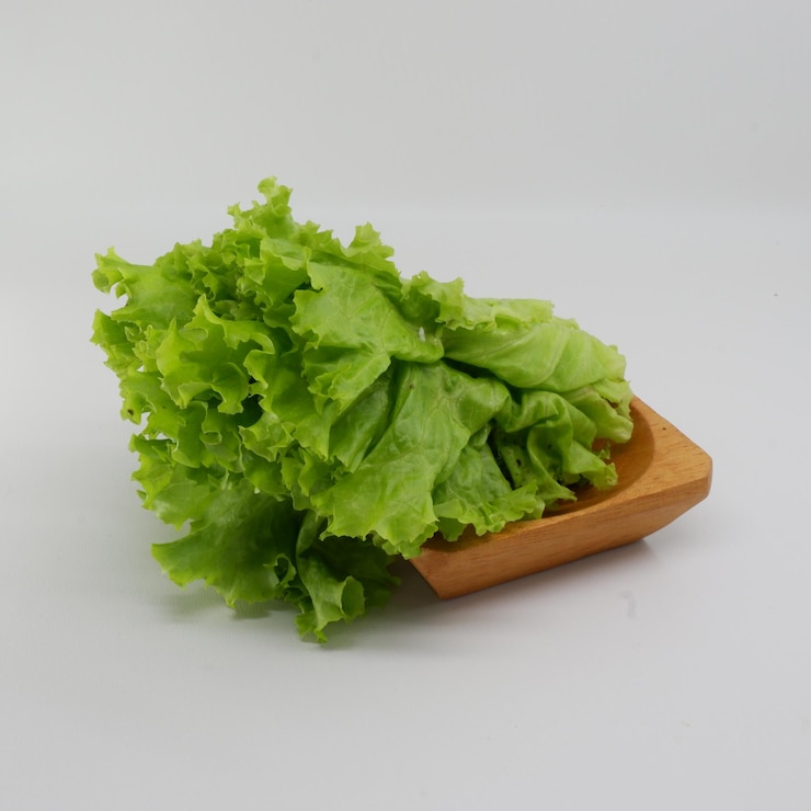 Foto una bandeja de madera con lechuga y un fondo blanco.