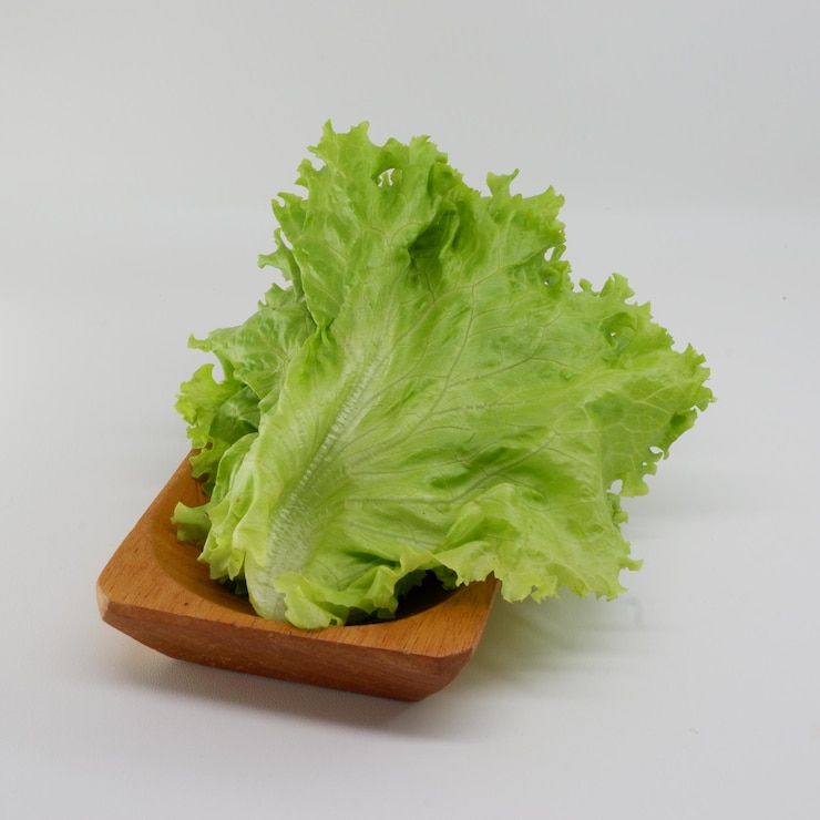 Foto una bandeja de madera con lechuga y un fondo blanco.