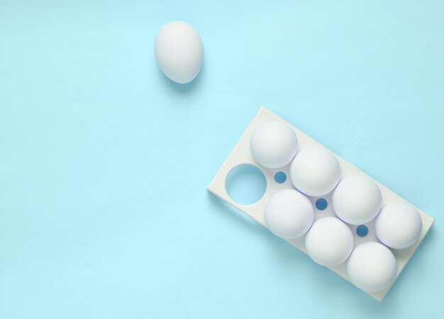 Bandeja de plástico con huevos blancos sobre fondo azul pastel, tendencia minimalista, vista superior