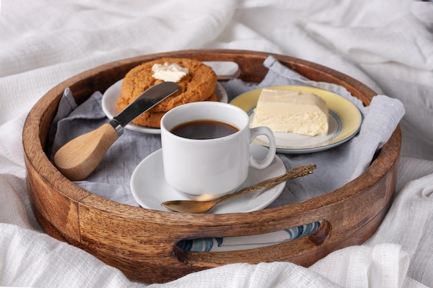 Bandeja redonda de madera con galletas de avena y mantequilla taza de desayuno de café negro en la cama