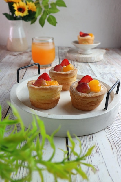 Una bandeja de tartas de frutas con un vaso de jugo de naranja al lado.