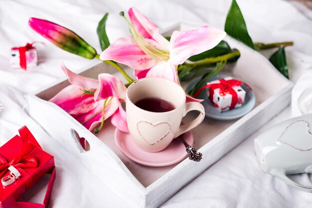 Bandeja con taza de té caliente en la cama.