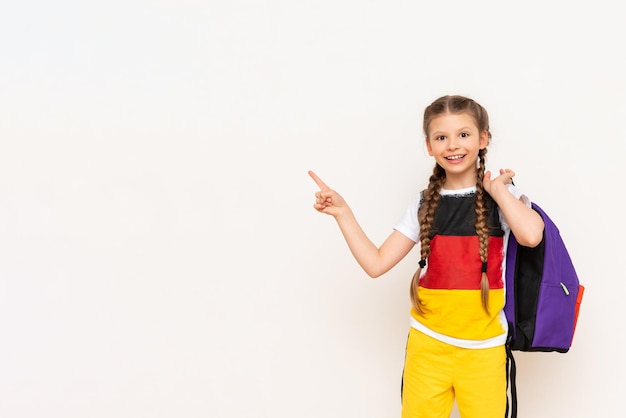 La bandera de Alemania en la camiseta de una niña Un hermoso niño con coletas apunta con su dedo índice a su anuncio sobre un fondo blanco aislado Cursos de idiomas para niños