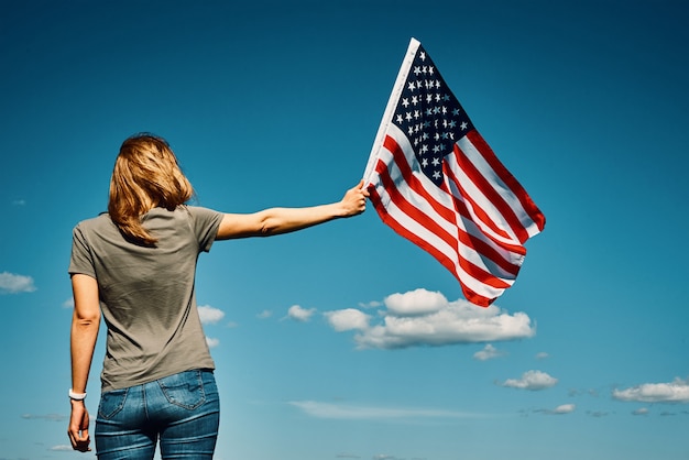 Bandera americana al aire libre mujer sostiene la bandera nacional de EE.UU. contra el cielo azul nublado el día de la independencia de julio