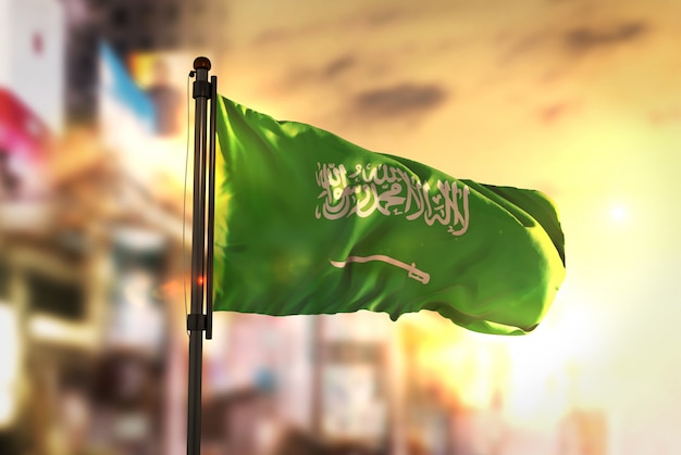 Bandera de Arabia Saudita contra la ciudad de fondo borroso a la luz del sol de fondo