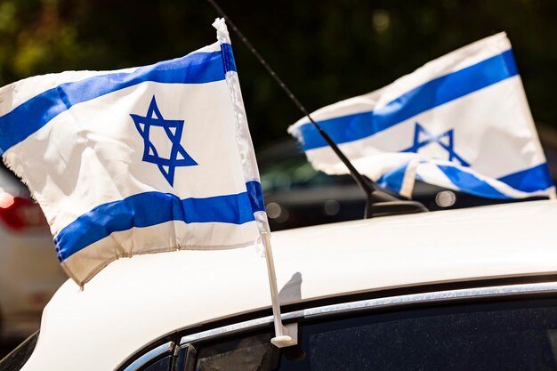 Bandera azul blanca israelí en la ventanilla de un automóvil ondeando el día de la independencia de Israel El automóvil con banderas nacionales israelíes pasa por la calle El concepto de celebración de la libertad patriotismo Banderas ondeando en el viento